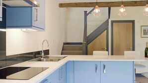 A modern kitchen with a built-in stove, a sink, and blue cabinets. There is a staircase leading to another level, and a wooden door is visible. - The Garden Room at Eudon George (Eudon George, near Bridgnorth)