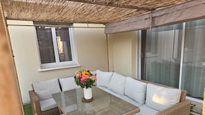 An outdoor seating area with a glass-top table, wicker furniture, and a flower vase.