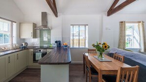 Una cuina moderna amb una illa central, bigues de fusta i una zona de menjador amb taula i cadires.