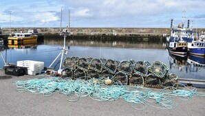 A harbor with boats docked, fishing nets, and a calm sea.