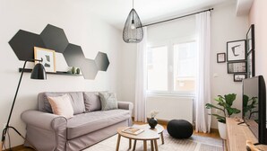 A modern living room with a grey sofa, a round wooden coffee table, and a black hanging light fixture. - Delightful 1BD Apartment in Plaka (Athens)