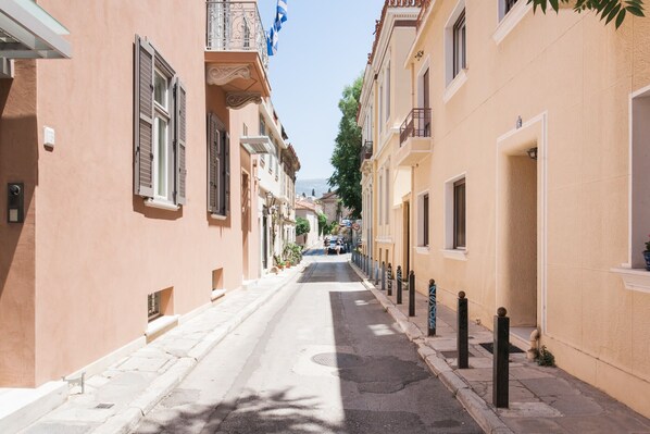 Une rue étroite bordée d’immeubles, dont certains sont dotés de balcons et de volets, et un ciel dégagé au-dessus.
