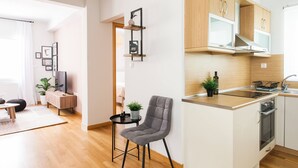 A modern apartment with a kitchen featuring wooden cabinets, a built-in oven, and a small dining area with a grey chair and a table. - Delightful 1BD Apartment in Plaka (Athens)