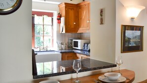 A modern kitchen with wooden cabinets, a granite countertop, and a dining area with a table set for two. - 1 bedroom accommodation in Slingsby, near Malton (Slingsby, near Malton)