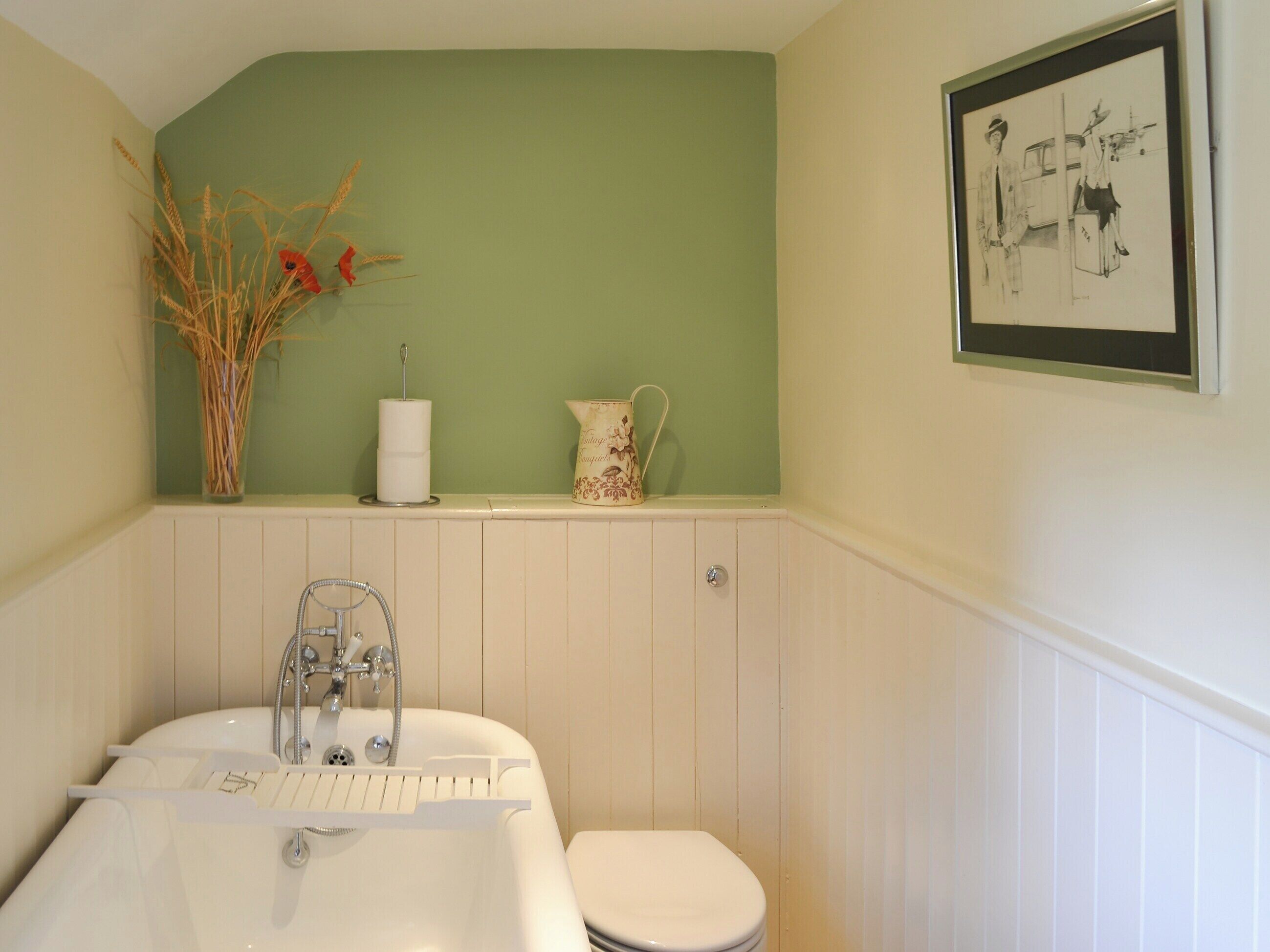 A bathroom with a white bathtub, a toilet, a sink, and a shelf with decorative items.