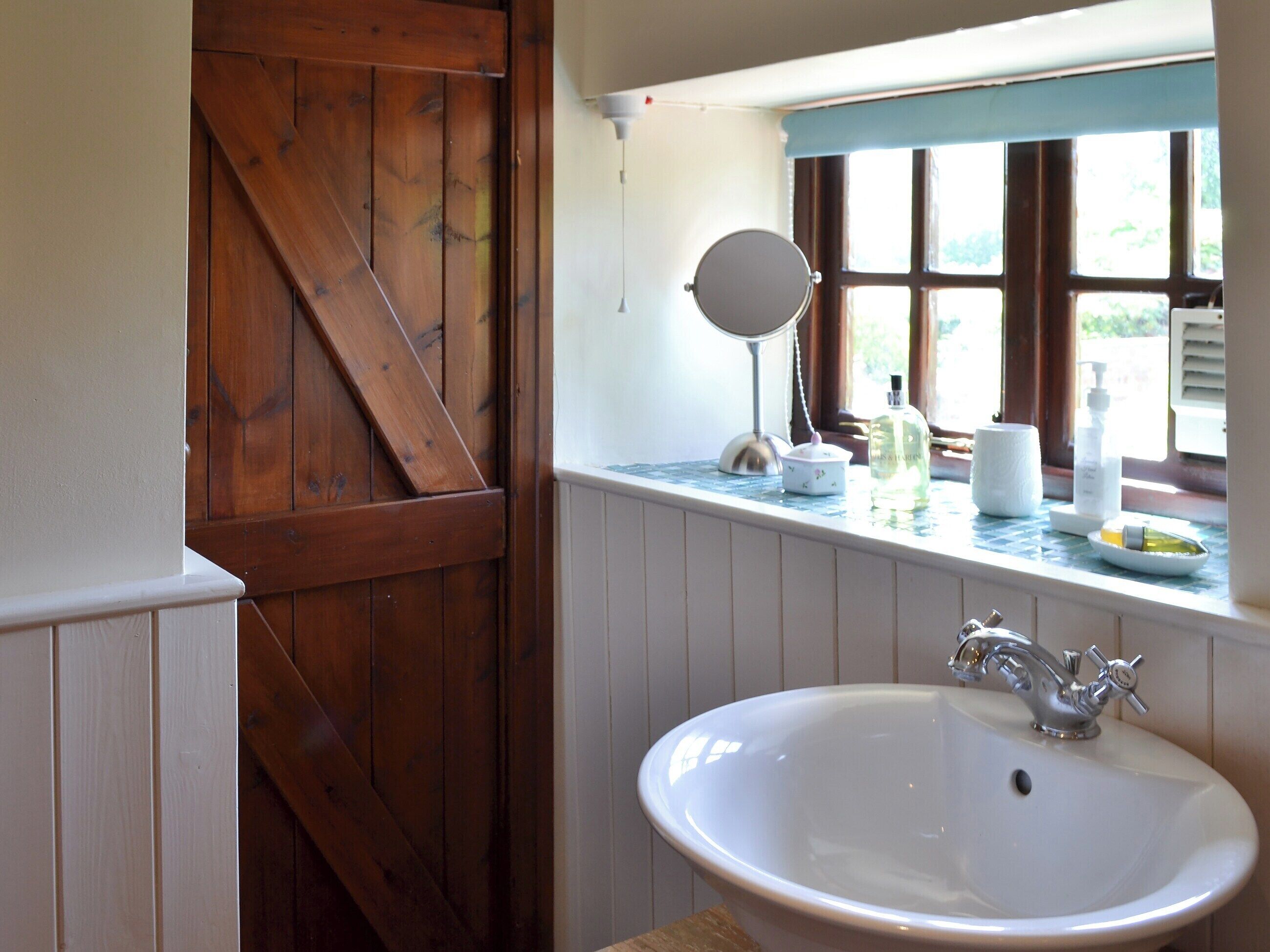 A bathroom with a wooden door, a white sink, a mirror, and toiletries on the windowsill.