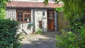 A stone house with a tiled roof, a wooden door, and a garden area with a hose and plants. - 1 bedroom accommodation in Slingsby, near Malton (Slingsby, near Malton)