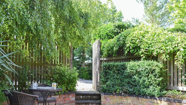 A patio with a table and chairs, surrounded by lush greenery and a wooden fence. - 1 bedroom accommodation in Slingsby, near Malton (Slingsby, near Malton)