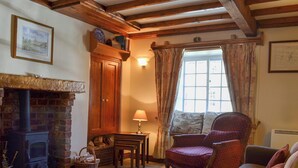 A cozy living room with a fireplace, a comfortable armchair, a sofa, and a window with curtains. - 1 bedroom accommodation in Slingsby, near Malton (Slingsby, near Malton)