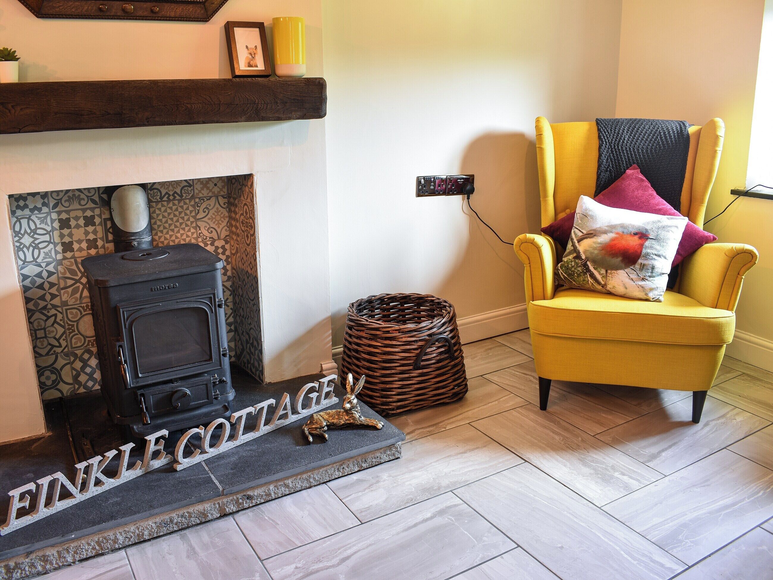 Una sala de estar acogedora con chimenea, un sillón amarillo y una cesta de mimbre.