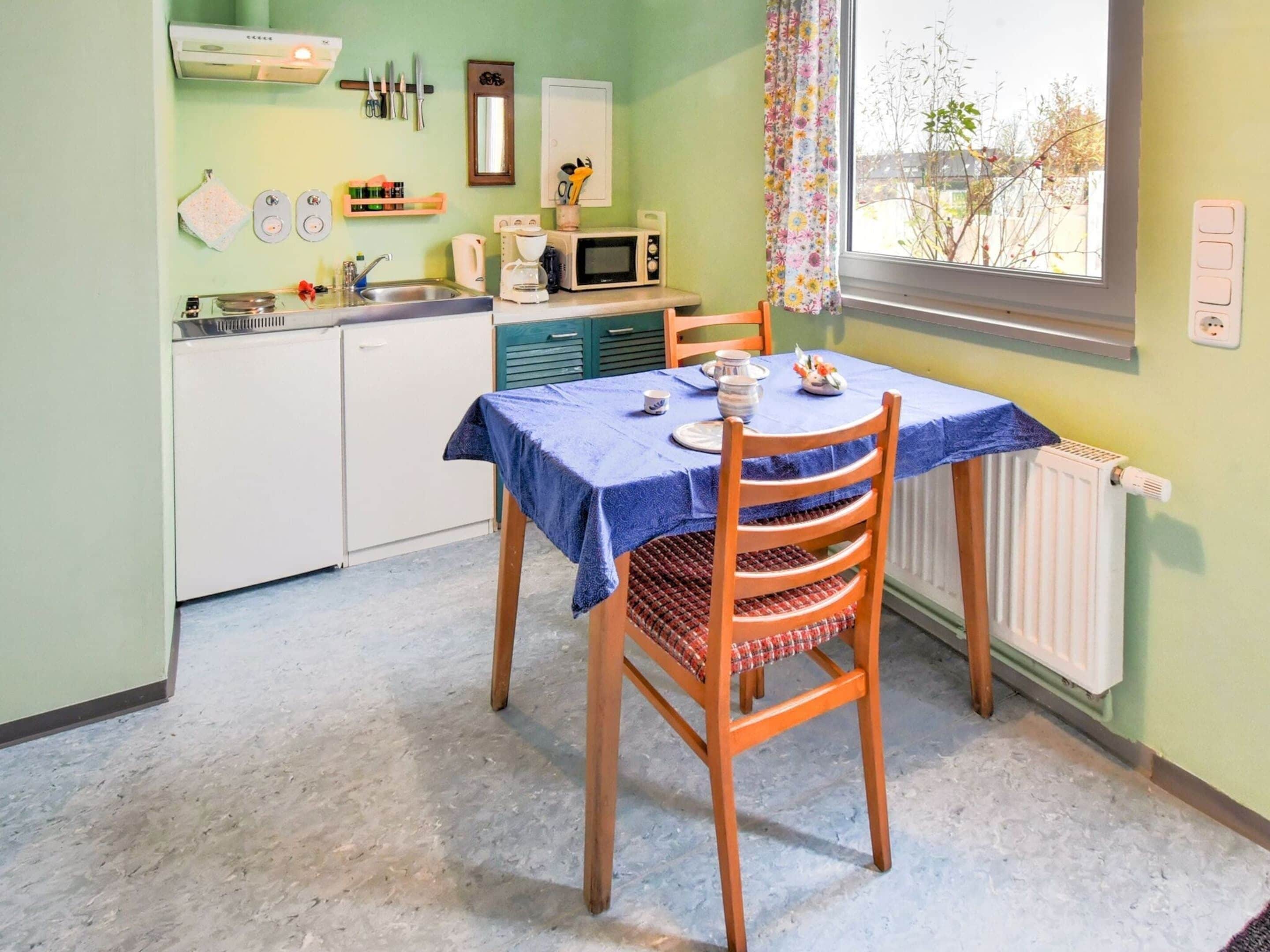Une petite cuisine avec une table dressée pour deux personnes, un four à micro-ondes et une fenêtre donnant sur les arbres.