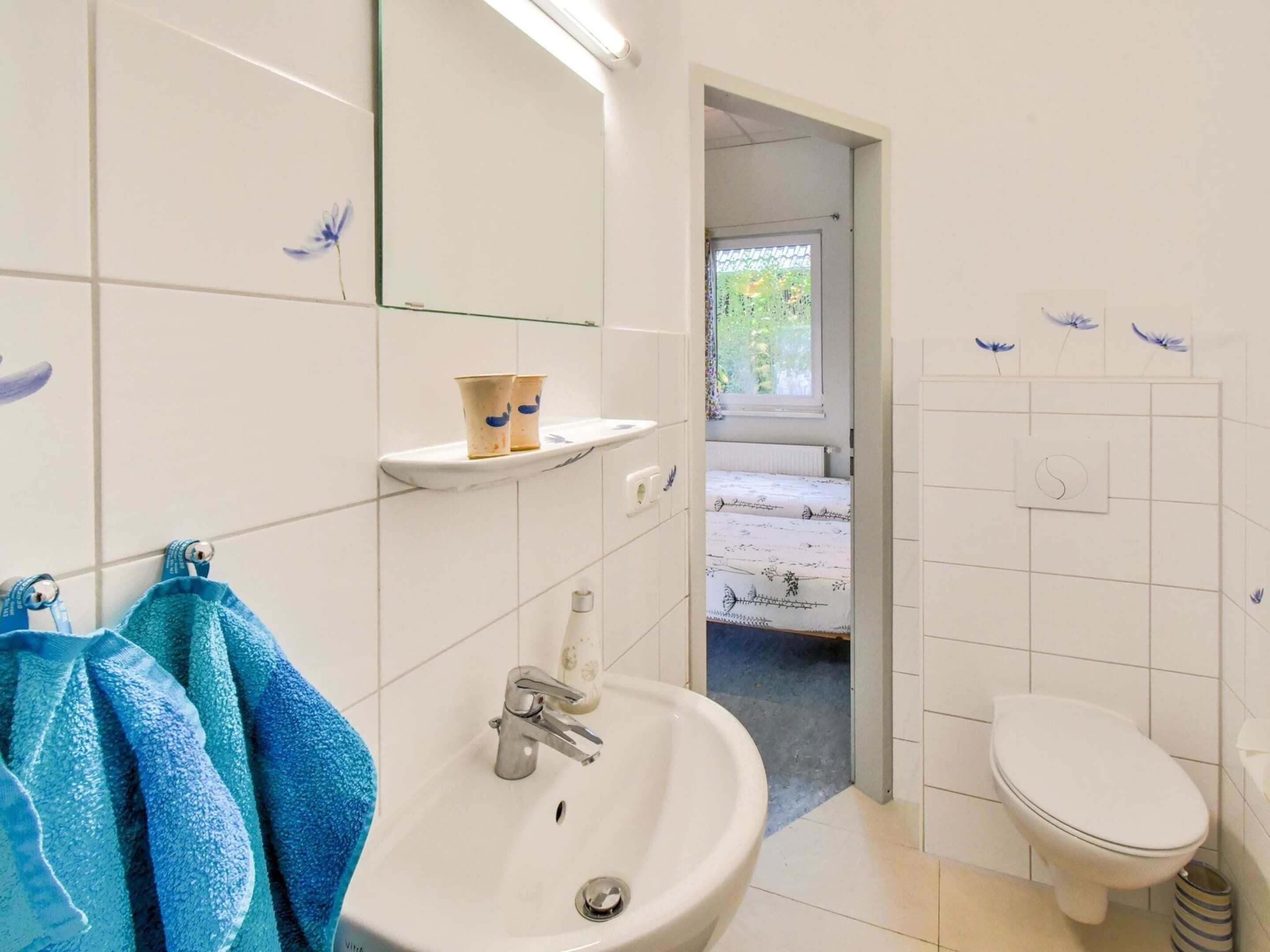 A bathroom with a sink, mirror, and toilet. There is a window with a view of greenery outside.