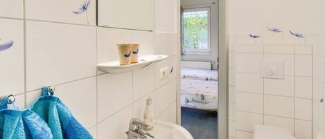 A bathroom with a sink, mirror, and toilet. There is a window with a view of greenery outside.