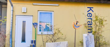 A yellow building with a tiled roof, a door, a window, and a sign that reads "Keram".