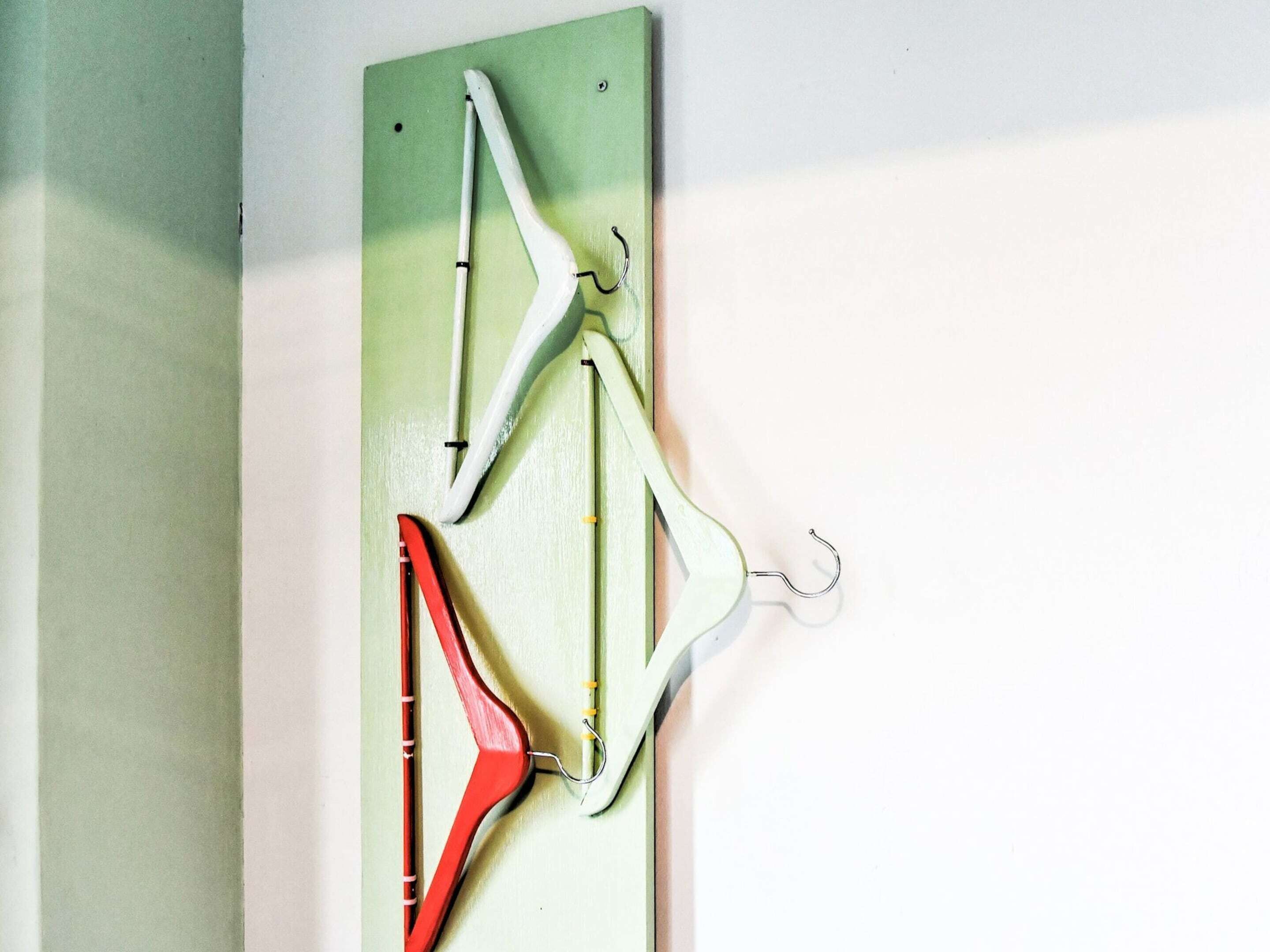 Un perchero de pared con varios ganchos, incluyendo un gancho rojo y dos blancos.