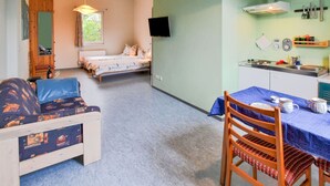 A compact room with a bed, a sofa, a dining table with chairs, a TV mounted on the wall, and a kitchenette area. - Nifty Apartment in Rövershagen near Sea (Roevershagen)