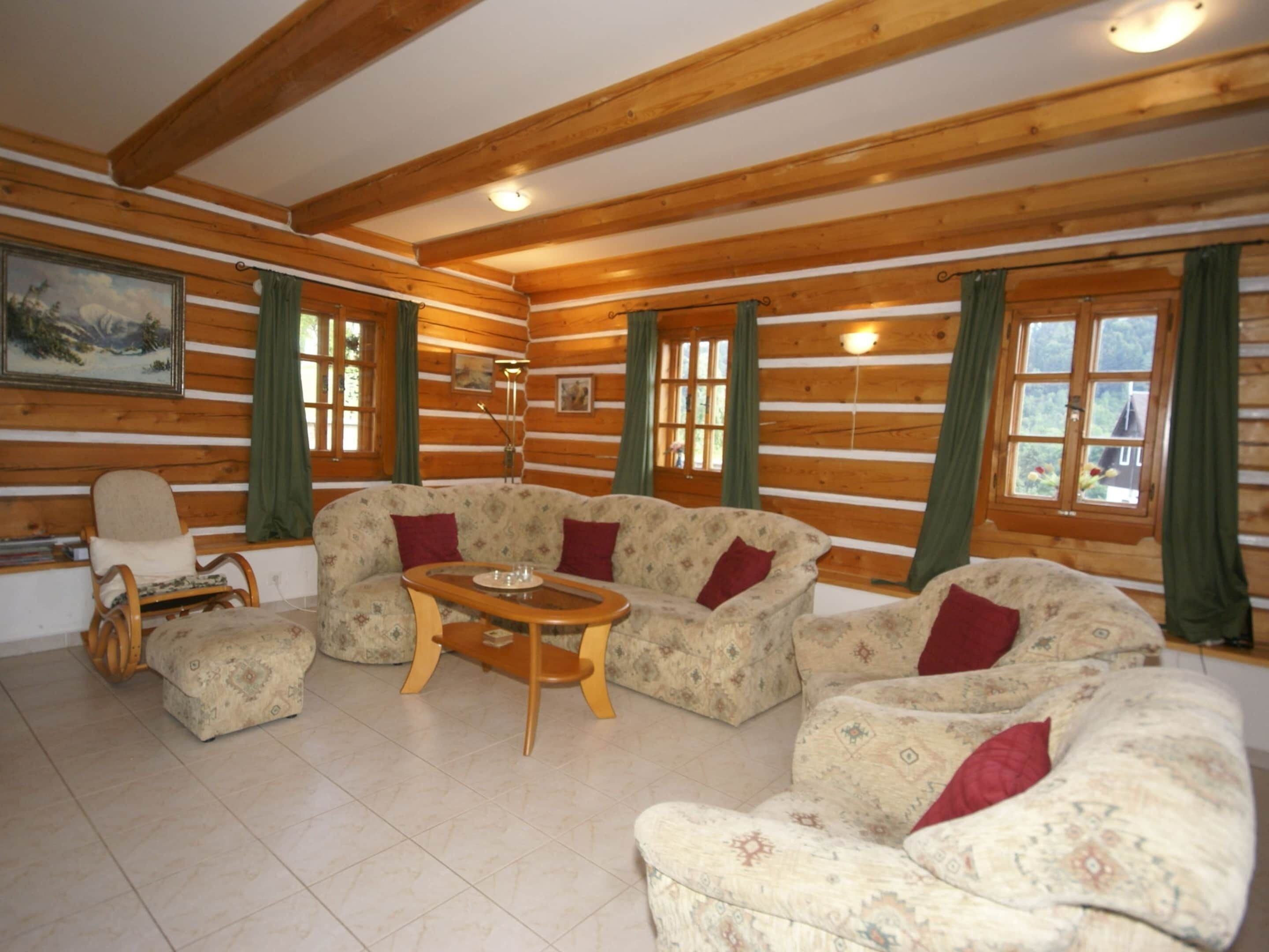 Interior de una cabaña de troncos con un sofá, una silla y una mesa.