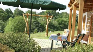 Una pérgola de madera con un paraguas verde, una mesa con mantel colorido y una silla con cojín.