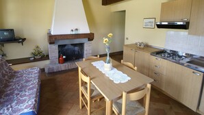Una cocina acogedora con chimenea, armarios de madera, una mesa de comedor con mantel de encaje y un sofá en la sala de estar.