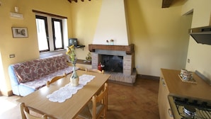 Una sala de estar acogedora con chimenea, un sofá, una mesa de comedor con sillas y una zona de cocina con estufa.
