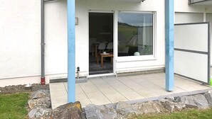 Un bâtiment doté d’un patio couvert, d’une porte-fenêtre coulissante donnant sur un espace intérieur avec une table et des chaises, et d’une porte de garage.