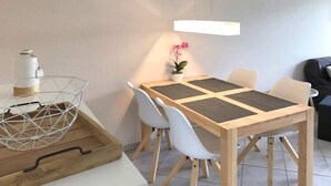 Un coin repas avec une table en bois, des chaises blanches, une petite plante en pot et un luminaire suspendu.