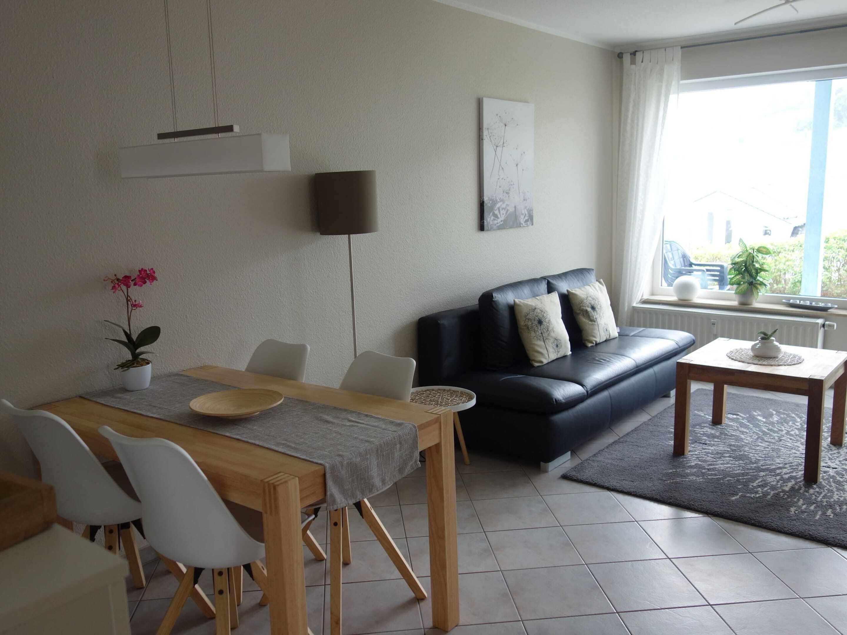 Ein modernes Wohnzimmer mit Essbereich, einem schwarzen Ledersofa, einem Holzesstisch und Blick ins Freie.