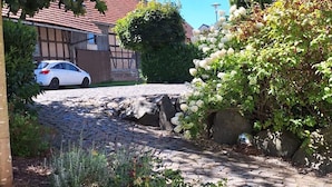 Uma passagem de calçada de pedra leva a um carro branco estacionado em frente a uma casa com telhado de telhas vermelhas.