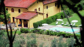 Un grand bâtiment jaune avec un toit recouvert de tuiles rouges, une piscine et un espace extérieur aménagé pour s’asseoir.