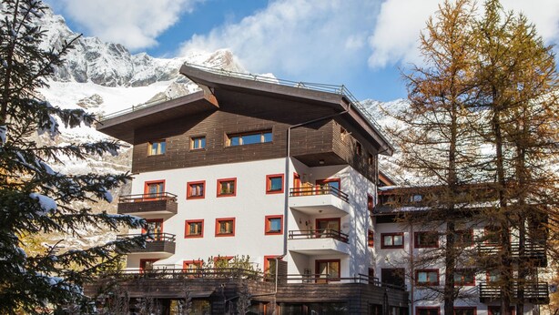 A multi-story hotel with balconies, a snow-covered ground, and mountains in the background. - Matterhorn View Apartment in Breuil-Cervinia near Ski Area (Valtournenche)