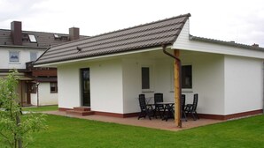 Una casa a un piano con un portico coperto, dotato di tavolo e sedie.