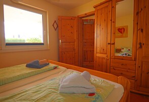 Un dormitorio con dos camas, armarios de madera, un ventanal y un espejo.