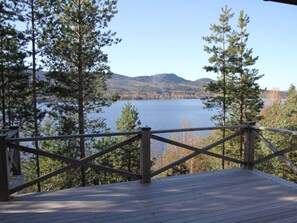 A wooden deck with a railing overlooking a lake surrounded by trees and hills. - Ski, Sauna, and Scandinavian Serenity Chalet (Torsby)