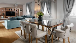 A modern living room with a glass-top dining table, six upholstered chairs, a blue sofa, a TV, and a chandelier. - 4-bed Villa With Pool in Vabriga (Tar-Vabriga)