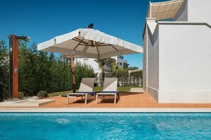 A swimming pool with two lounge chairs and a large umbrella.