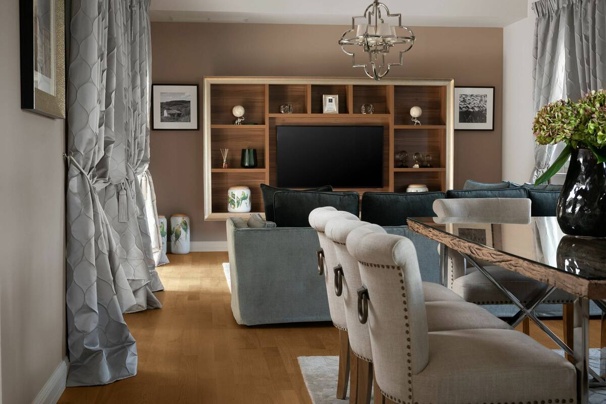 A living room with a sofa, ottoman, and chairs, a TV, wooden shelves, and a chandelier.