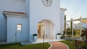 A white building with a large clock on the wall, a covered entrance, and a brick pathway leading to the door. - 4-bed Villa With Pool in Vabriga (Tar-Vabriga)