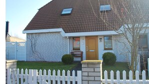 Une maison avec un toit recouvert de tuiles brunes, une clôture blanche en bois et une façade en briques.