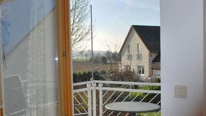 Un balcon avec une table et des chaises, donnant sur un quartier résidentiel avec des maisons et un ciel dégagé.