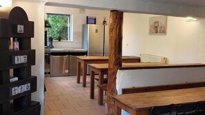 A dining area with wooden tables and chairs, a refrigerator, and a shelf with decorative items. - Modern Holiday Home with Hot Tub & Sauna in Ardennes (Lierneux)