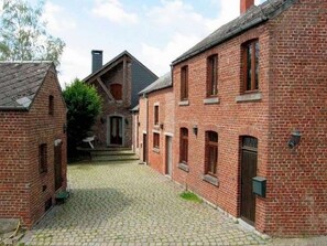 A courtyard with red brick buildings, cobblestone path, and a central building with a gabled roof.
