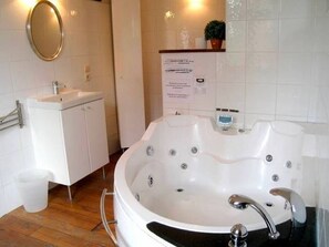 A bathroom with a white sink, a mirror, a white bathtub with multiple jets, and a small potted plant on the counter.