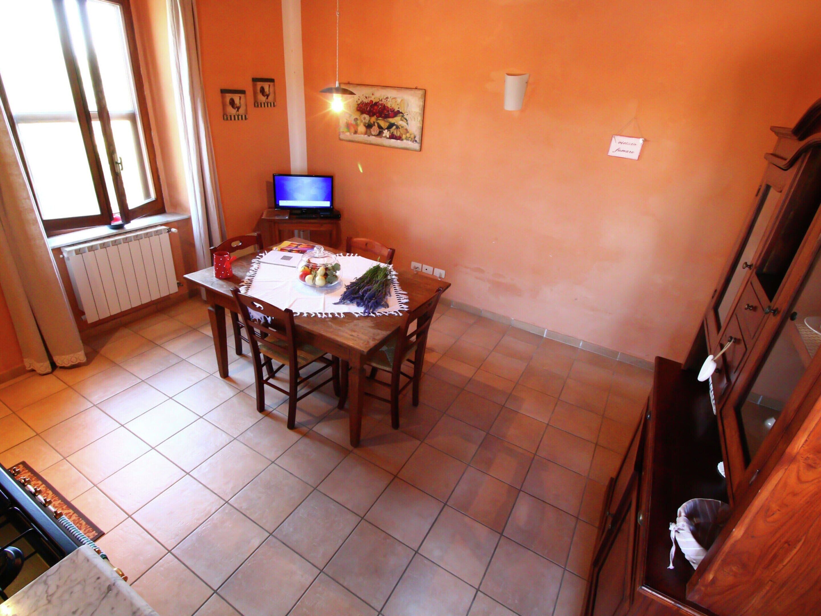 A dining area with a table set for two, a radiator, a television, and a window with curtains.