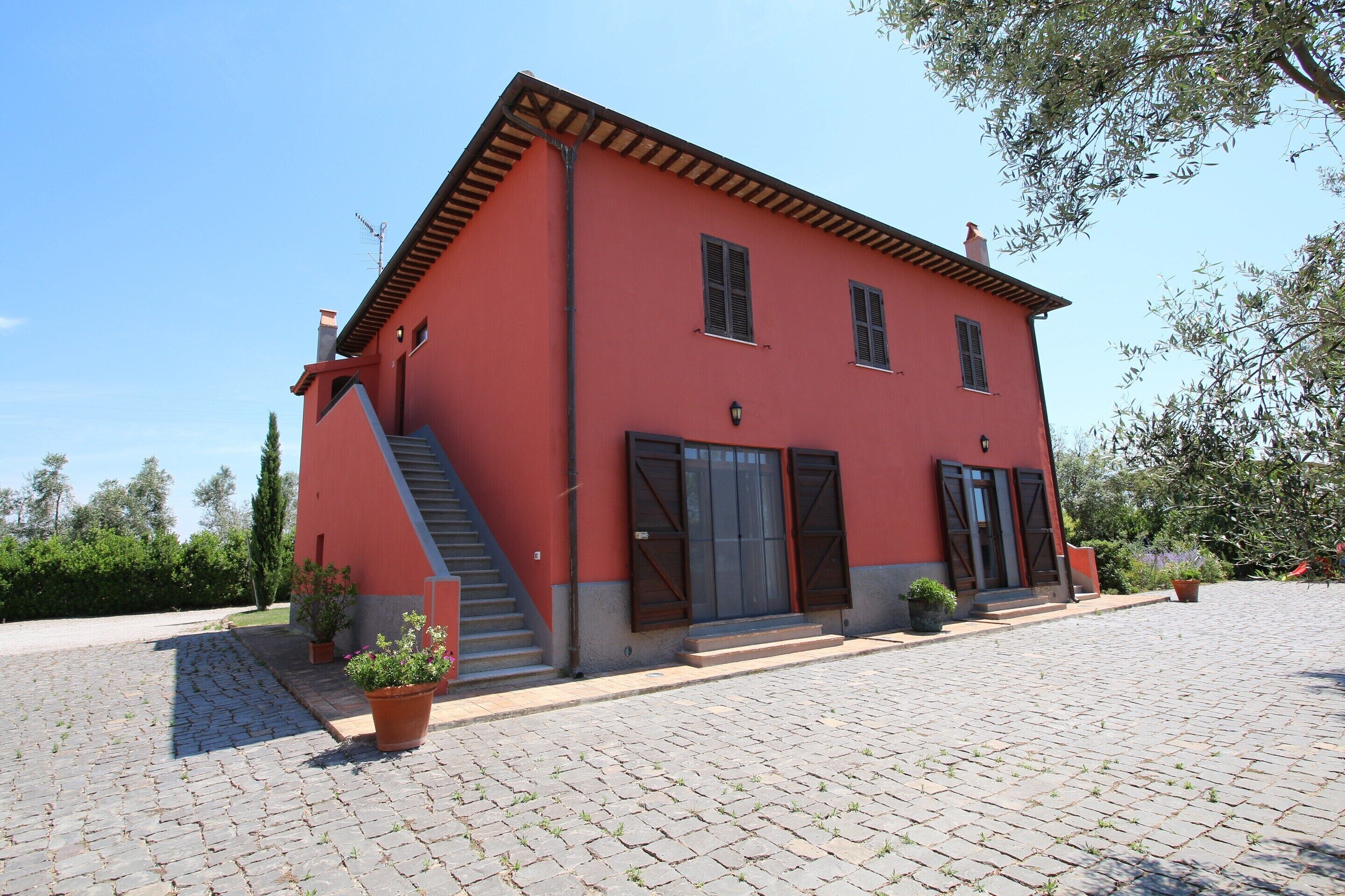A red building with a staircase, potted plants, and a paved courtyard.