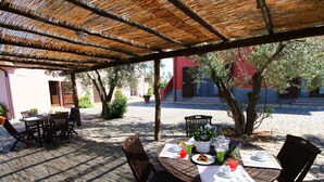 An outdoor café with tables and chairs under a shaded pergola, surrounded by cobblestone pavement and trees. - Apartment in Montalto Near Lake and Pool (Montalto di Castro)