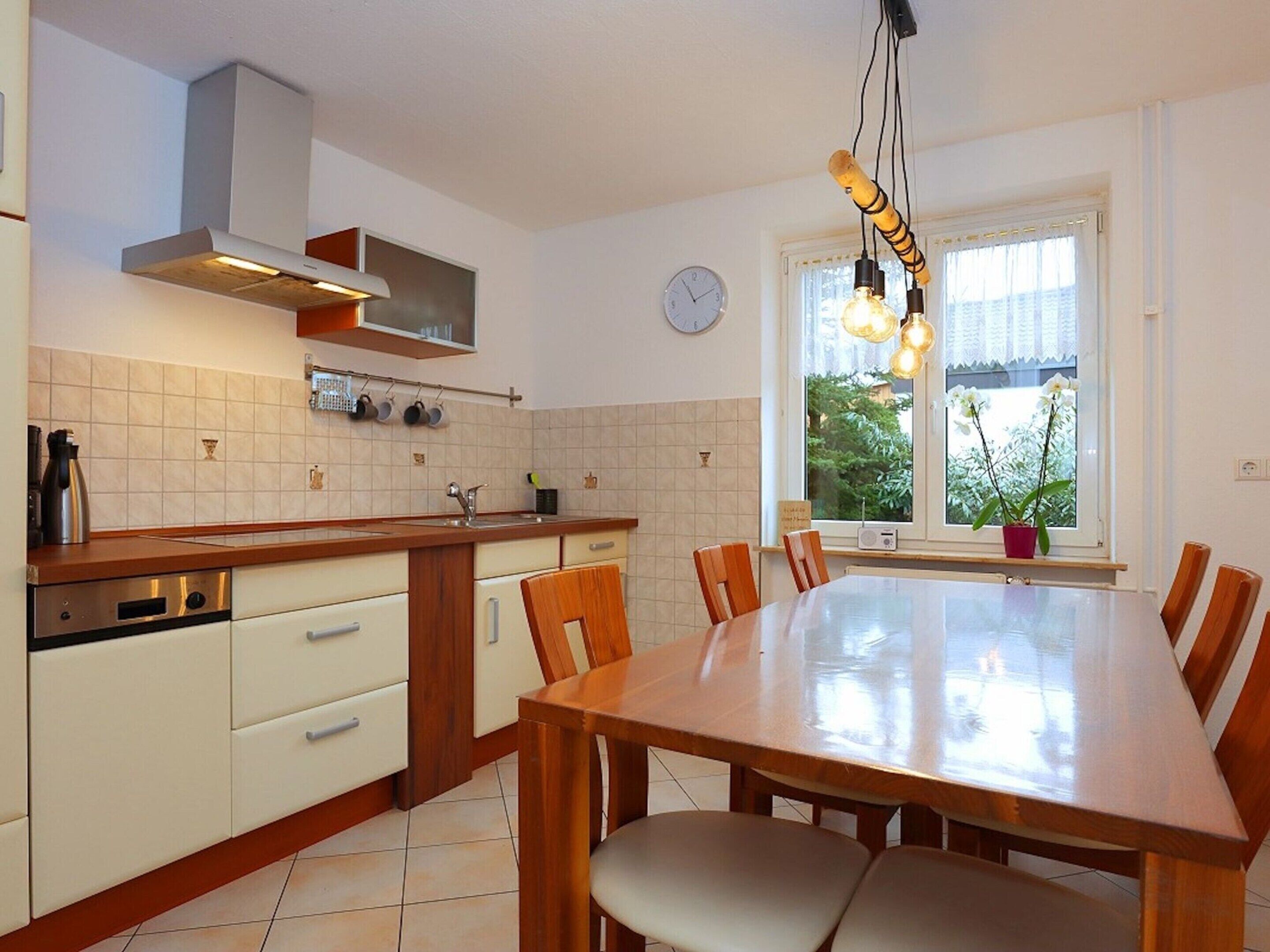 Cozinha moderna com mesa e cadeiras de madeira, forno embutido e janela com vista para vegetação.