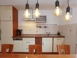 Una cocina con armarios blancos, encimera de madera, pileta doble y cuatro sillas de madera.
