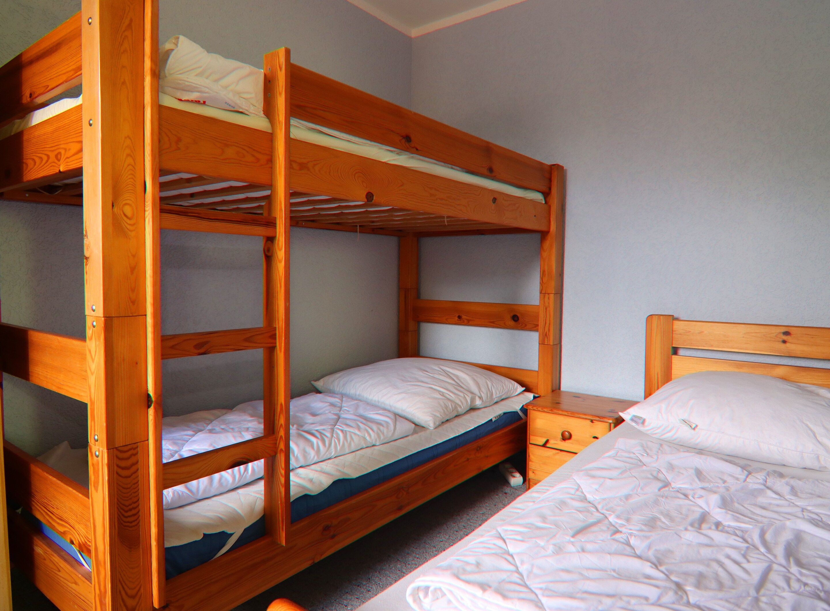 A bunk bed with two levels, a wooden nightstand, and a single bed.