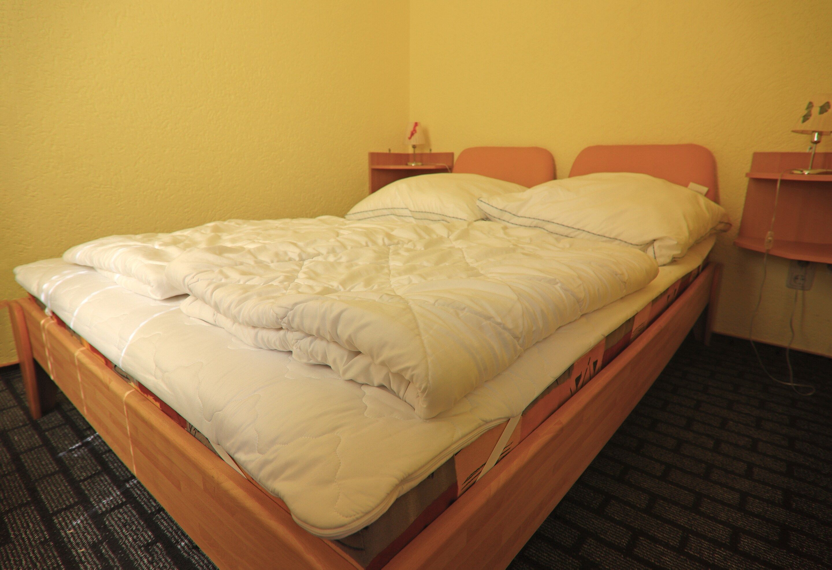 Ein Einzelbett mit weißer Bettdecke und Kissen, ein Holz-Kopfteil und ein Boden mit Ziegeloptik.