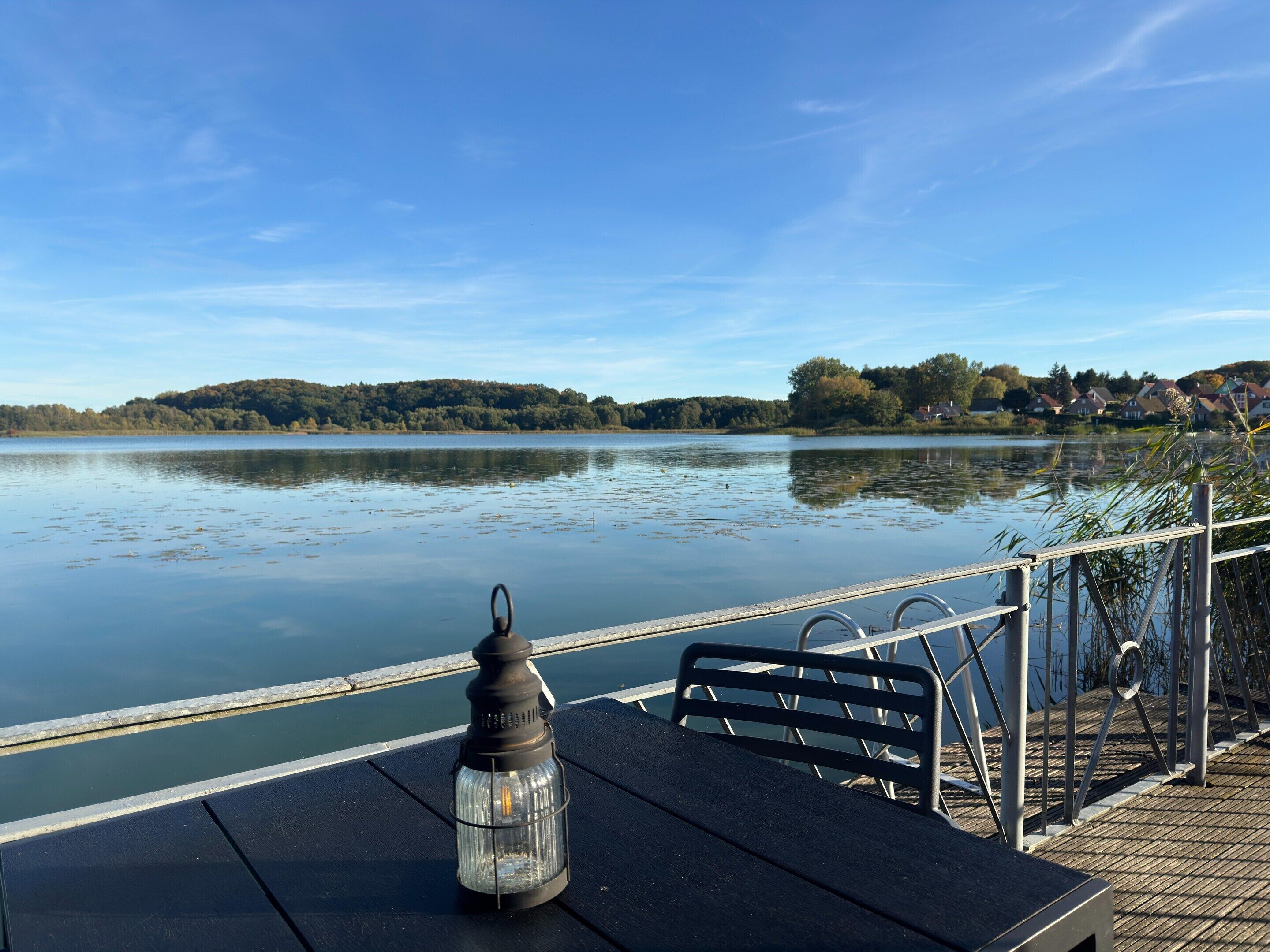 Blick auf einen See mit Tisch und Stühlen, einer Laterne und einem Geländer mit Blick aufs Wasser.